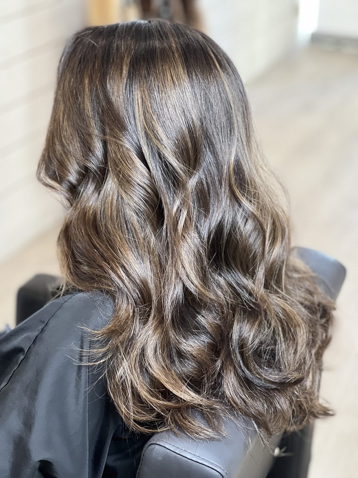 Glossy dark brunette balayage with caramel ribbons and loose waves